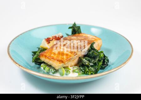 Appetitliches gegrilltes Lachsfilet mit knuspriger Kruste und Grillspuren wird auf einem türkisfarbenen Keramikteller mit Spinat, grünen Erbsen, Zitronenscheibe und re Stockfoto