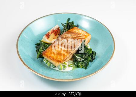 Gegrilltes Lachsfilet mit grünen Erbsen und Spinat auf einem türkisfarbenen Teller, Studioaufnahme. Stockfoto