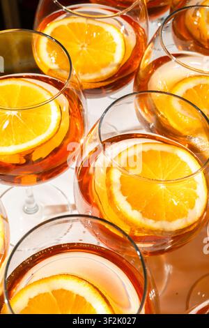 Gläser gefüllt mit einem bernsteinfarbenen Cocktail und frischen Orangenscheiben werden in einer Nahaufnahme unter hellem Studiolicht für eine Premium-Getränkepräsentation eingefangen Stockfoto