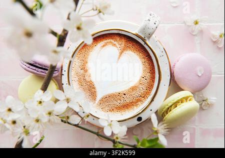 Kaffee mit herzförmigem Muster und süße Makronen-Desserts Ein rosa Kachelhintergrund Stockfoto