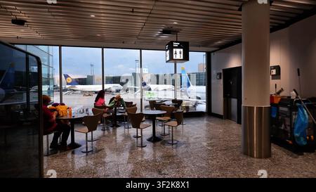 FRANKFURT, DEUTSCHLAND - 15. MAI 2024: Passagiere sitzen in einem Wartebereich am Flughafen Frankfurt und blicken durch große Fenster auf Flugzeuge, die auf dem Stockfoto