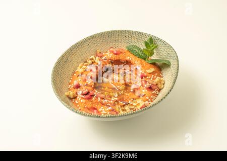 Libanesischer Muhammara-Dip mit Walnüssen, Granatapfelkernen und Sesam, garniert mit frischer Minze in einer strukturierten Steinzeugschale. Stockfoto