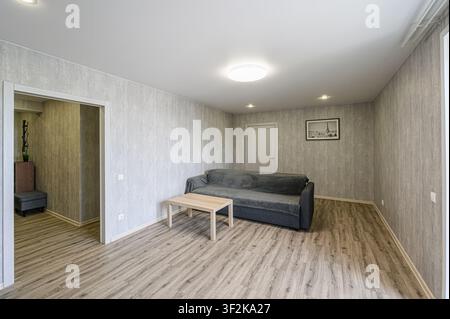 modernes Wohnzimmer mit einem grauen Sofa, Holztisch und holzgemusterten Böden. Neutrale Farbgebung Stockfoto