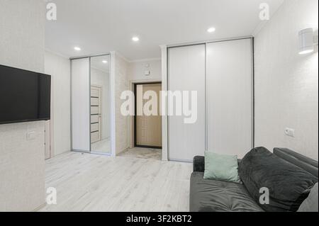 Heller Raum mit einem dunklen Sofa, hellen Böden, Schiebetürschränken und einem Fernseher. Innentüren sind sichtbar Stockfoto