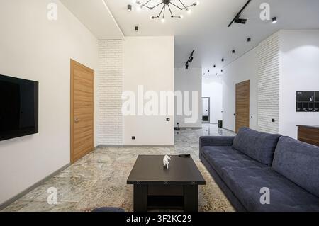 modernes Wohnzimmer mit einem blauen Sofa, dunklem Couchtisch und stilvoller Beleuchtung Stockfoto