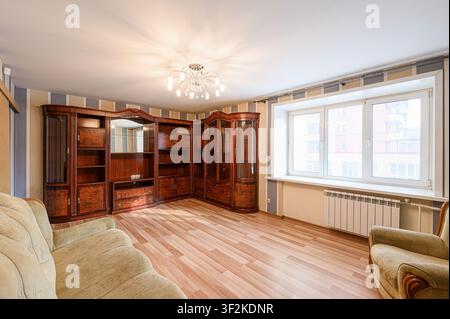 Wohnzimmer mit einer großen hölzernen Unterhaltungsanlage, einem Sofa und einem Fenster mit einer Heizung Stockfoto