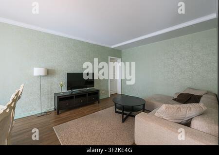 Gemütliches Wohnzimmer mit gemusterten Wänden, Fernseher, Sofa, Teppich und rundem Tisch. Eine Lampe sorgt für sanfte Beleuchtung Stockfoto