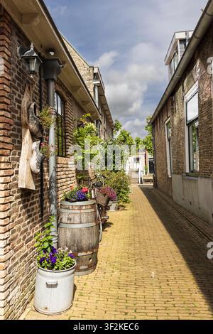 Eine sonnige schmale Ziegelgasse, gesäumt von Blumenkästen, Holzfässern und einem Vintage-Fahrrad im historischen Sloten, Friesland, Niederlande, zeigt cha Stockfoto