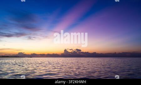 Farbenfroher Sonnenuntergang über dem ruhigen Indischen Ozean in der Nähe von Maamigili Island, Malediven, mit lila Wolken, die sich über dem ruhigen Wasser spiegeln. Stockfoto