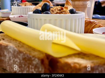 Frühstücksessen im Café am Tisch, gebratenes Ei, gelber Eigelb in der Bratpfanne, Käscheiben, Croissant und frische Beeren in einer Schüssel. Dep Stockfoto