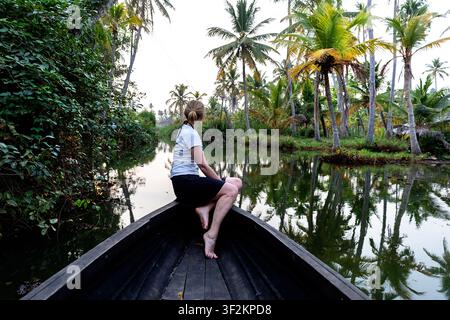 Touristin sitzt auf einem traditionellen Holzboot und erkundet die malerischen Wasserkanäle der Munroe-Insel in den Backwaters von Kerala, Indien. Stockfoto
