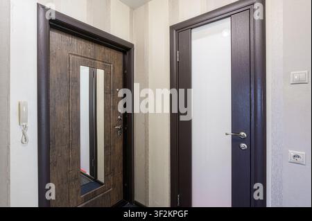 Zwei Türen stehen nebeneinander. Eine ist aus Holz mit einem Spiegel, die andere hat eine Milchglasscheibe. Die Wände sind neutral Stockfoto