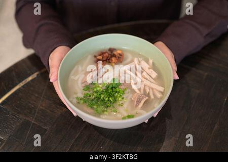 Eine Nahaufnahme-Horizontalaufnahme, die sich auf eine hellgrüne Keramikschale konzentriert, die mit einer tröstlichen Nudelsuppe gefüllt ist, gehalten von einer Person in dunklem Braun Stockfoto