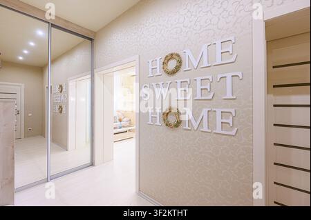 Eine gemütliche Innenszene mit einem Flur und einem Spiegelschrank. Der Spruch „HOME SWEET HOME“ ist an der Wand dargestellt, wobei die „O“s von Kränzen gebildet werden. Neutra Stockfoto