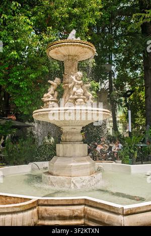 Batumi, Georgien – 09. Juni 2026: Antike Steinfontäne mit geschnitzten Puttenstatuen und verziertem Becken in einem öffentlichen Park, umgeben von üppigen Bäumen. Stockfoto