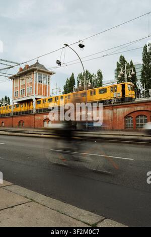 Berlin, Deutschland, 15.07.26, Ein gelber Berliner U-Bahn-Zug passiert die erhöhte Schlesisches Tor-Station in Berlin-Kreuzberg, Deutschland, während ein Radfahrer sich bewegt Stockfoto