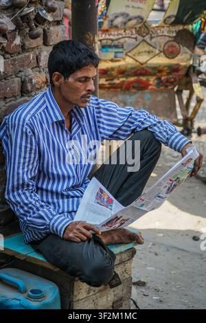 Dhaka, Bangladesch - 26. Februar 2017: Ein Mann mit dunklem Haar und Schnurrbart, der ein blau-weiß gestreiftes Langarmhemd und dunkle Hosen trägt, sitzt ba Stockfoto
