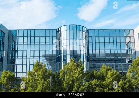 Moderne Glasfassade eines Bürogebäudes in der Nähe der Hackerbrücke in München, Bayern, mit metallener Sonnenschutzstruktur und grünen Bäumen im Vordergrund. Hochwertige p Stockfoto
