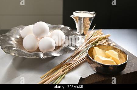 Frische Eier, Butter, Milch und Weizen, die auf einem rustikalen Küchentisch als Zutaten für hausgemachtes Kunsthandwerk-Brot arrangiert sind Stockfoto