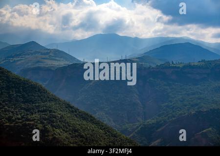 Schroffe Bergkette, bedeckt mit dichtem grünen Wald. Sonnenlicht bricht durch die Wolken über den Gipfeln. Tiefe Täler und steile Hänge schaffen ein dramatisches Gelände Stockfoto