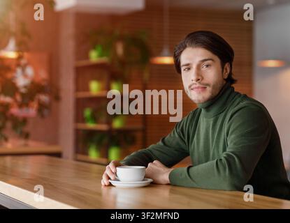 Junger schöner Mann, der allein im Café sitzt und Kaffee trinkt Stockfoto