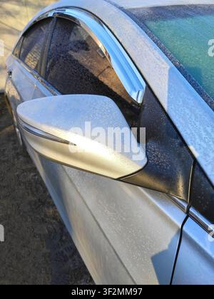 Nahaufnahme eines silbernen Autospiegels und mit Frost und Eiskristallen bedeckter Fenster an einem kalten Wintermorgen. Saisonales Wetter, Gefrieratemperatur Stockfoto