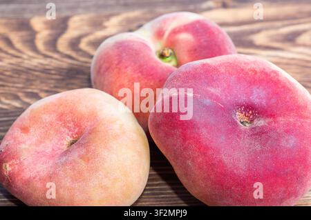 Drei flache Saturn-Pfirsiche in einer Nahaufnahme, angeordnet auf einem dunklen strukturierten Holz Hintergrund. Stockfoto