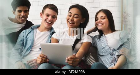 Vier junge Freunde, glücklich lächelnd, die zusammen zu Hause ein Video auf einem Tablet anschauen, Lifestyle-Konzept Stockfoto