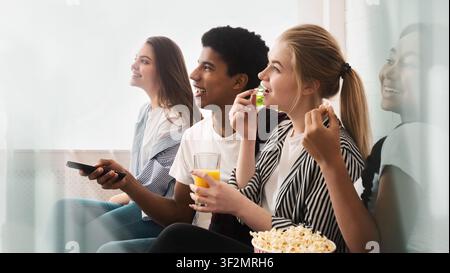 Gruppe junger Leute genießt Filmabend zu Hause, lächelnd und Snacks essend Stockfoto