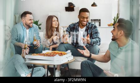 Gruppe von Freunden genießt Pizza und Getränke zu Hause, fröhliche Lächeln, lockere Zusammenkunft Stockfoto