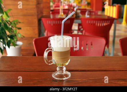 Der Kaffee Latte Macchiato mit Sahne verziert, serviert in einem hohen Glas mit Henkel und Stern auf einem schönen Holztisch in einem abstrakten Straßenkaffee Stockfoto