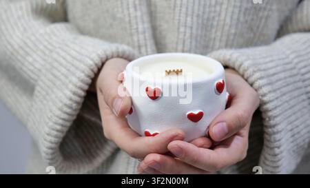Frau hält eine weiße Kerze mit roten Herzen in einem gestrickten Pullover Stockfoto