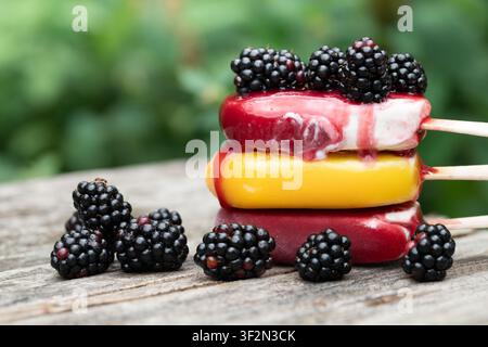 Drei Eis am Stiel sind übereinander auf einem rustikalen Holzbrett gestapelt. Die Eis am Stiel beginnen zu schmelzen. Es gibt Brombeeren oben drauf und ne Stockfoto