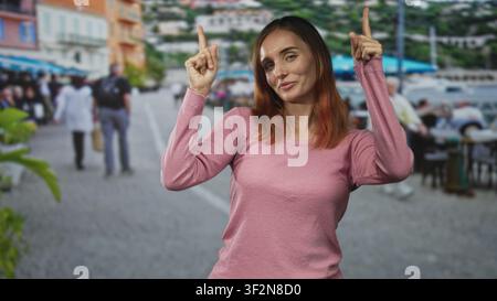 Frau zeigt beide Zeigefinger nach oben und zeigt Finger und Handflächen auf einer belebten Straßenpromenade; hoffe Neugier. Stockfoto