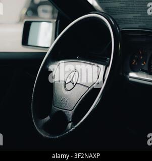 Nahaufnahme eines dunklen ästhetischen Shoots eines klassischen Mercedes-Benz-Lenkrads, wobei der Fokus auf dem strukturierten Leder, dem Mittelhupenpolster und dem ikonischen Sternemblem liegt Stockfoto