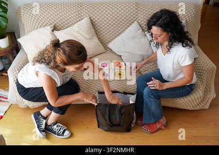 Hohe Blickwinkelansicht von zwei kreativen Freundinnen, die in eine schwarze Tasche mit handgefertigten Textilhandwerken schauen Stockfoto