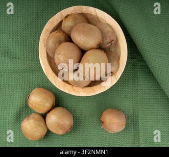 Kiwis auf dem Tisch. Stapel grüner Kiwis, pelziger Kivi in einer Schale, frische saftige tropische Früchte mit Samen, Kiwi auf grünem Tischtuchhintergrund von oben Stockfoto