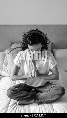Vertikale Aufnahme einer friedlichen Frau in Lotussitzhaltung, die ein Headset zur Meditation nutzt Stockfoto