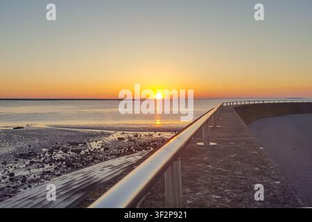 Ein malerischer Blick auf die untergehende Sonne am Horizont in Burnham on Sea, die ein warmes Licht über das ruhige Meer wirft Stockfoto