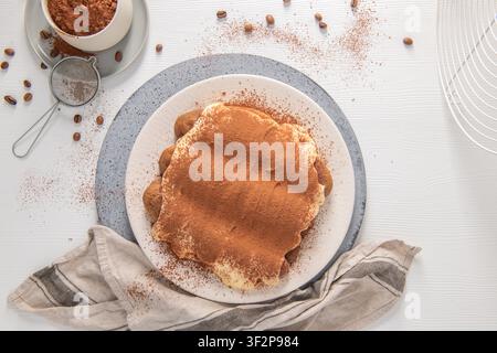 Eine Top-Down-Ansicht eines köstlichen hausgemachten Tiramisu, das auf einem modernen Teller serviert wird, umgeben von Kakaopulver und Kaffeebohnen. Generative KI. Stockfoto