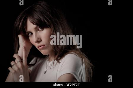 Porträt einer nachdenklichen jungen Frau, die ihren Kopf mit einem dunklen Hintergrund hält Stockfoto