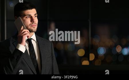 Junger Geschäftsmann, Der Bei Nacht Im Büro Telefonieren Kann Stockfoto