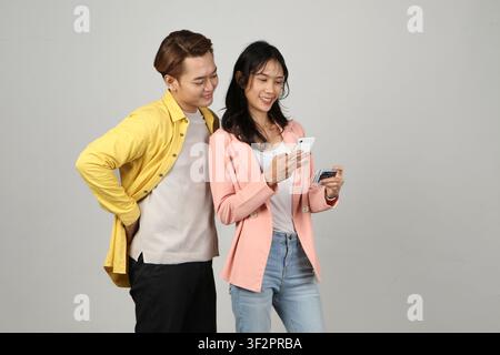 Porträt eines glücklichen asiatischen indonesischen Paares, das ein Smartphone und eine Kreditkarte auf einem isolierten Hintergrund hält. Stockfoto