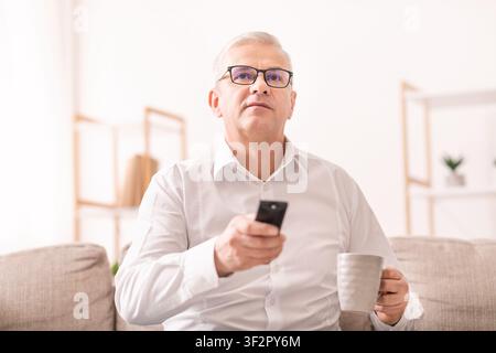 Älterer Mann, der Fernsehen mit Tee auf dem Sofa sieht Stockfoto