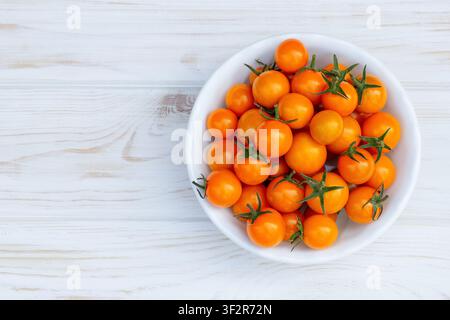 Voller weißer Keramikschüssel mit helloranger Kirschtomaten, Sorte Sungold, auf dem weißen rustikalen Holztisch. Stockfoto