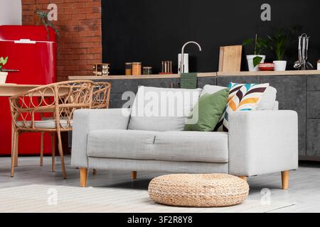 Modernes Wohn- und Esszimmer im offenen Grundriss mit grauer Couch, rotem Kühlschrank und Rattanstühlen Stockfoto