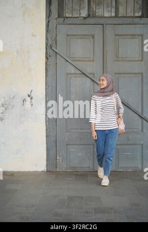 Asiatische muslimische Frau steht vor einer alten großen Holztür Stockfoto