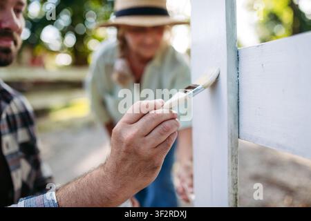 Erwachener Sohn und ältere Mutter arbeiten auf dem Bauernhof, malen den Zaun. Stockfoto