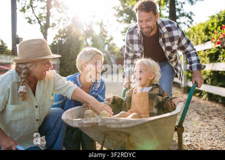 Fröhliches Kind im Schubkarren, Familienporträt auf dem Bauernhof. Stockfoto