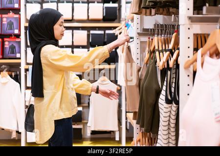 asiatische indonesische muslimische Frau mit Hijab, die im Einkaufszentrum Kleidung einkauft Stockfoto